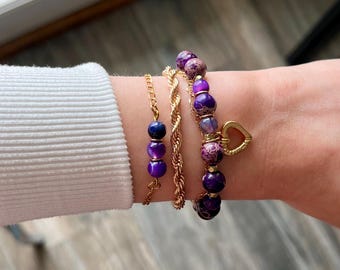 May include: A set of four bracelets featuring purple and gold beads. One bracelet has a heart charm.