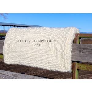 Könnte beinhalten: Ein weißer Woll-Teppich mit Fransen, der über einen Holzzaun gelegt ist. Der Teppich trägt den Text "Priddy Beadwork & Tack".