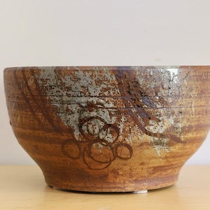May include: A brown ceramic bowl with a white glaze and a design of circles. The bowl has a wide rim and a rounded base.