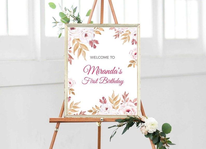 May include: A white sign with a gold frame and floral border. The sign says "Welcome to Miranda's First Birthday" in pink lettering.