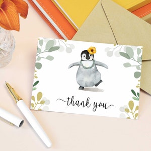 May include: A thank you card featuring a watercolour illustration of a penguin wearing a flower and a lei. The card has a green and gold floral border and the text "thank you" in cursive.