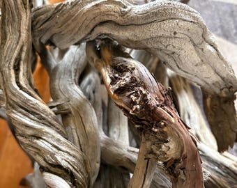 May include: A collection of weathered driftwood branches featuring twisted, gnarled textures and a mix of bleached gray and deep reddish-brown bark. The wood displays intricate grooves, knots, and organic shapes formed by natural erosion.
