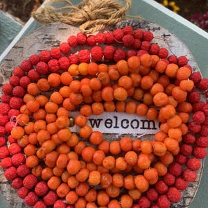May include: A wooden pumpkin-shaped sign with a welcome sign in the center. The sign is decorated with a wreath of red and orange berries.