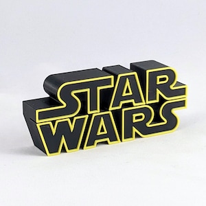 May include: Black plastic "Star Wars" logo with yellow lettering.