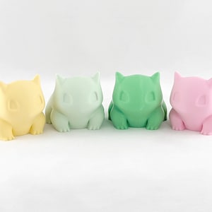 Puede incluir: Cuatro pequeñas figuritas de colores pastel de una criatura de dibujos animados. Las figuritas son amarillas, verde claro, verdes y rosas.