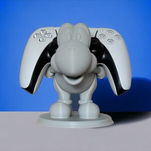 May include: A white 3D printed figurine of a cartoon character holding two white and black PlayStation 5 controllers.