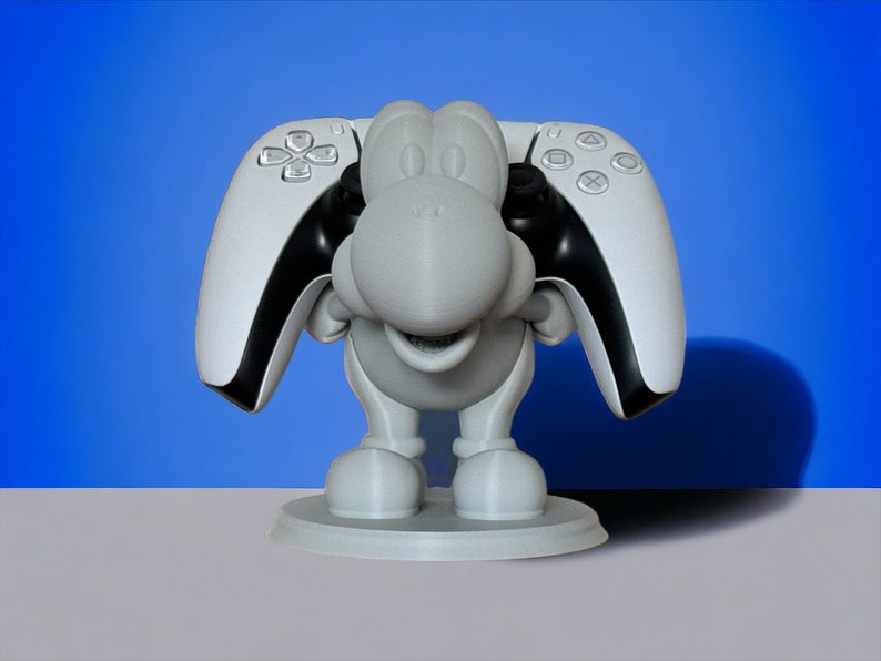May include: A white 3D printed figurine of a cartoon character holding two white and black PlayStation 5 controllers.