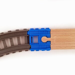 K&ouml;nnte beinhalten: Nahaufnahme eines Spielzeug-Eisenbahn-Gleissatzes mit einem blauen Kunststoff-Verbindungsst&uuml;ck und einem Holz-Gleisst&uuml;ck. Das Gleis besteht aus grauem Kunststoff und das Verbindungsst&uuml;ck hat ein Loch in der Mitte.