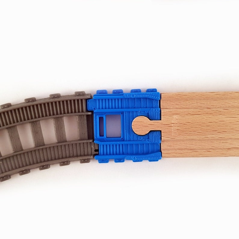K&ouml;nnte beinhalten: Nahaufnahme eines Spielzeug-Eisenbahn-Gleissatzes mit einem blauen Kunststoff-Verbindungsst&uuml;ck und einem Holz-Gleisst&uuml;ck. Das Gleis besteht aus grauem Kunststoff und das Verbindungsst&uuml;ck hat ein Loch in der Mitte.