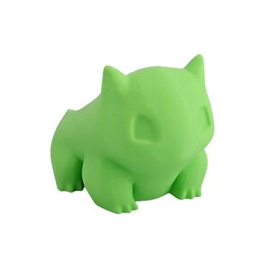 May include: A green plastic figurine of a cartoon character with large eyes and a rounded body.