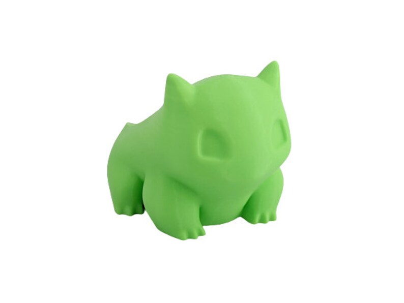May include: A green plastic figurine of a cartoon character with large eyes and a rounded body.