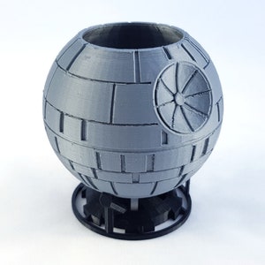 May include: A gray 3D printed Death Star planter with a black base. The planter is shaped like the Death Star from Star Wars.