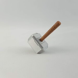 May include: A silver-colored toy hammer with a brown wooden handle. The hammer is shaped like Thor's hammer, Mjolnir.