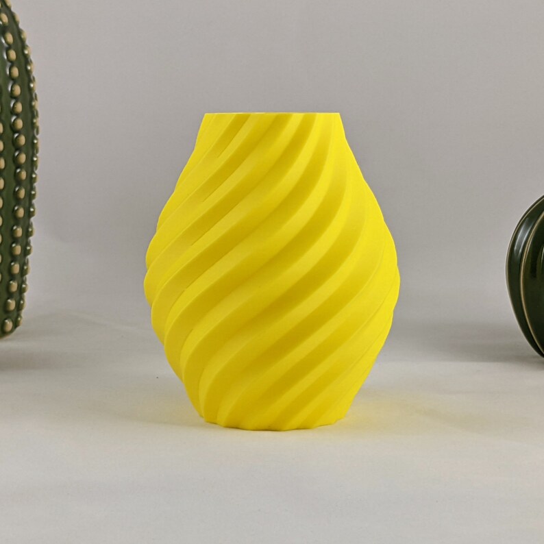 May include: A yellow ceramic vase with a swirling, textured design. The vase is a modern, contemporary style.