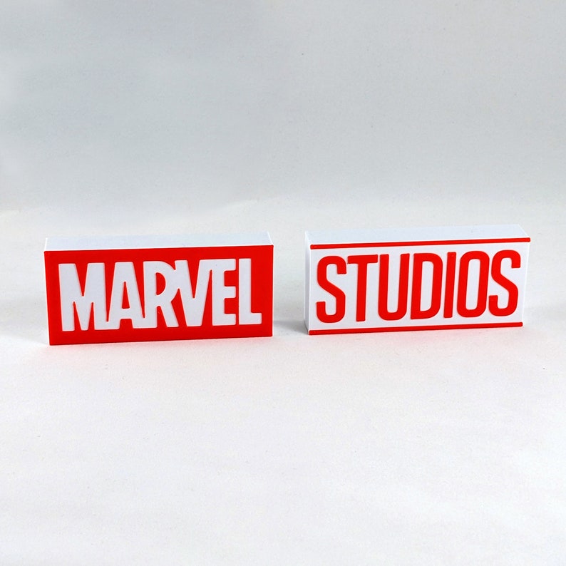 K&ouml;nnte beinhalten: Zwei wei&szlig;e rechteckige Bl&ouml;cke mit roter Beschriftung. Der erste Block sagt "MARVEL" und der zweite Block sagt "STUDIOS".