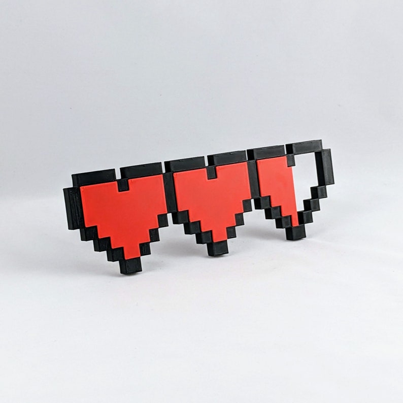 May include: A black and red pixelated heart health bar with three hearts, two full and one half full.