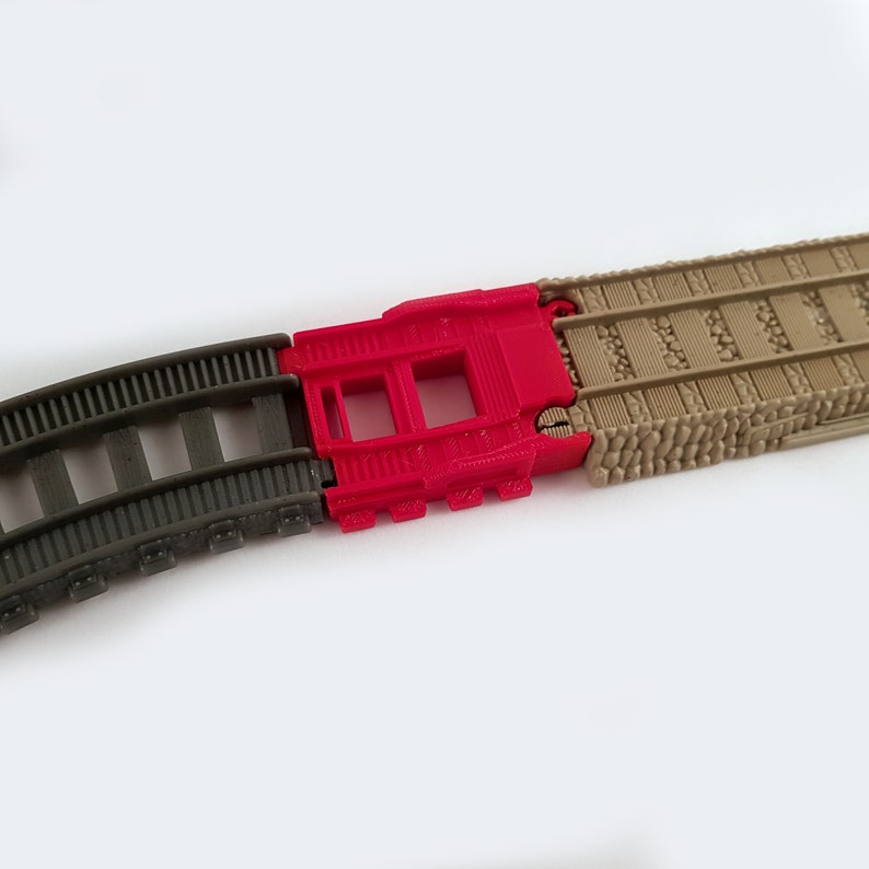 May include: Three pieces of plastic train track, one curved piece in dark gray, one straight piece in red, and one straight piece in tan.