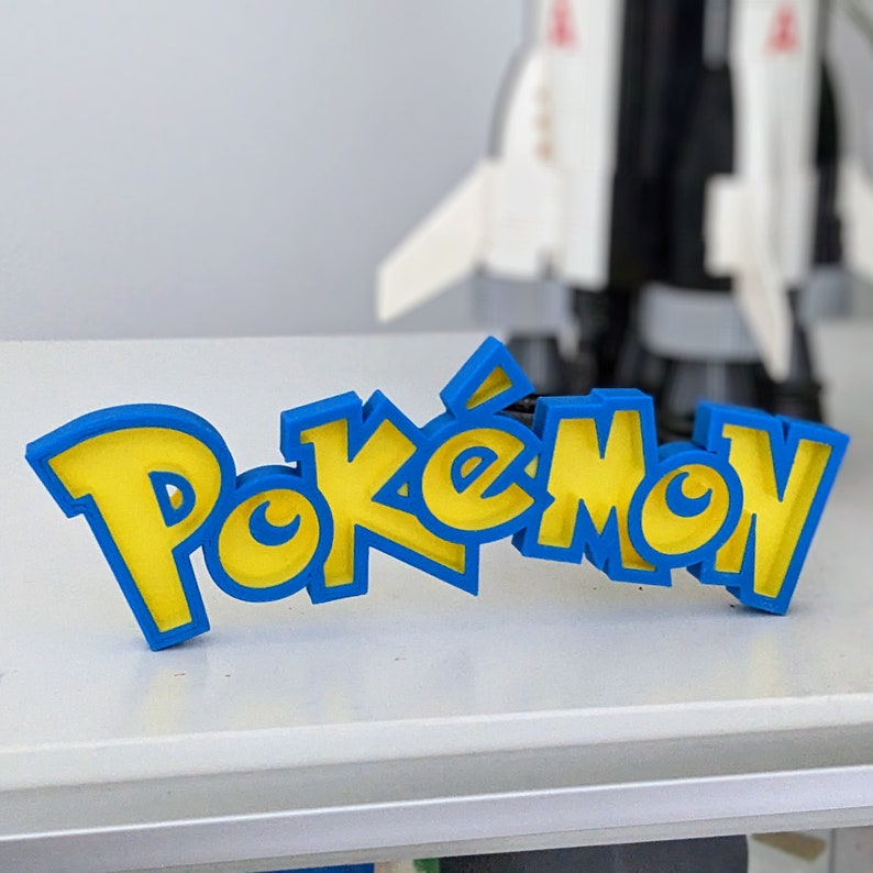 May include: A blue and yellow 3D printed sign that reads "Pokemon".