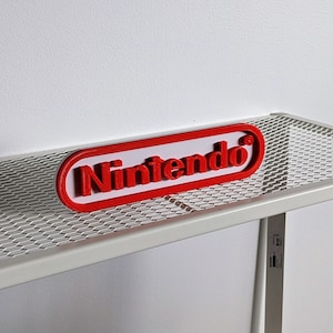 May include: A red 3D printed "Nintendo" logo on a white metal shelf with a wire mesh top.
