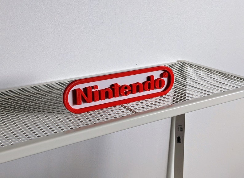 May include: A red 3D printed "Nintendo" logo on a white metal shelf with a wire mesh top.