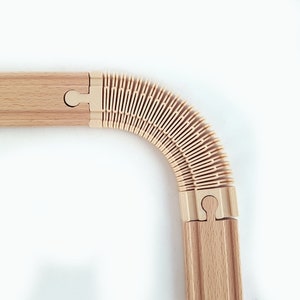 May include: A wooden train track set with a flexible, expandable section. The track is made of natural wood and has a light brown color. The flexible section is made of a cream-colored plastic.