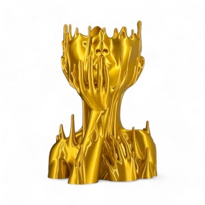 May include: A gold-coloured, abstract sculpture of a human head with hands covering the face. The sculpture is made of a smooth, flowing material that resembles melted metal.