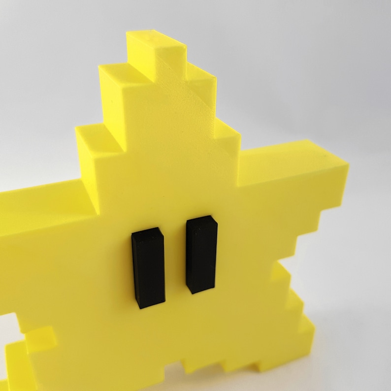 May include: A yellow pixelated star with two black rectangular eyes. The star is a 3D printed object.