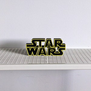 May include: Black and yellow 3D block letters spelling "STAR WARS" on a white surface.