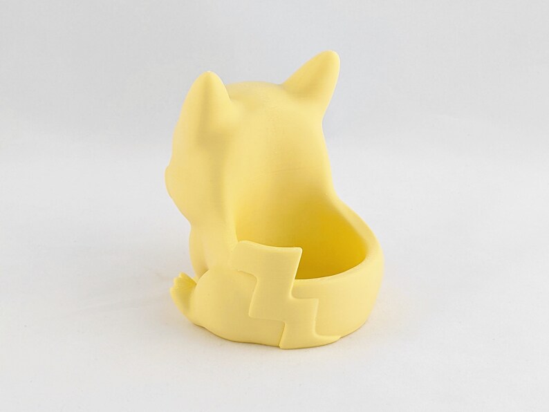 May include: A yellow ceramic planter shaped like a cartoon character sitting with its legs crossed. The planter has a small opening on the back for planting.