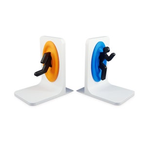 May include: A pair of white bookends shaped like portals from the video game Portal. One portal is orange and the other is blue. Each portal has a black figure of a person stepping through it.