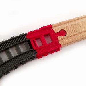 K&ouml;nnte beinhalten: Nahaufnahme einer Holz-Eisenbahnstrecke mit einem roten Kunststoff-Verbindungsst&uuml;ck. Das Verbindungsst&uuml;ck hat zwei rechteckige &Ouml;ffnungen.