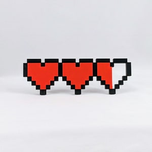 May include: Three pixelated hearts, two full and one half-full, in red with black outlines. The hearts are arranged horizontally.