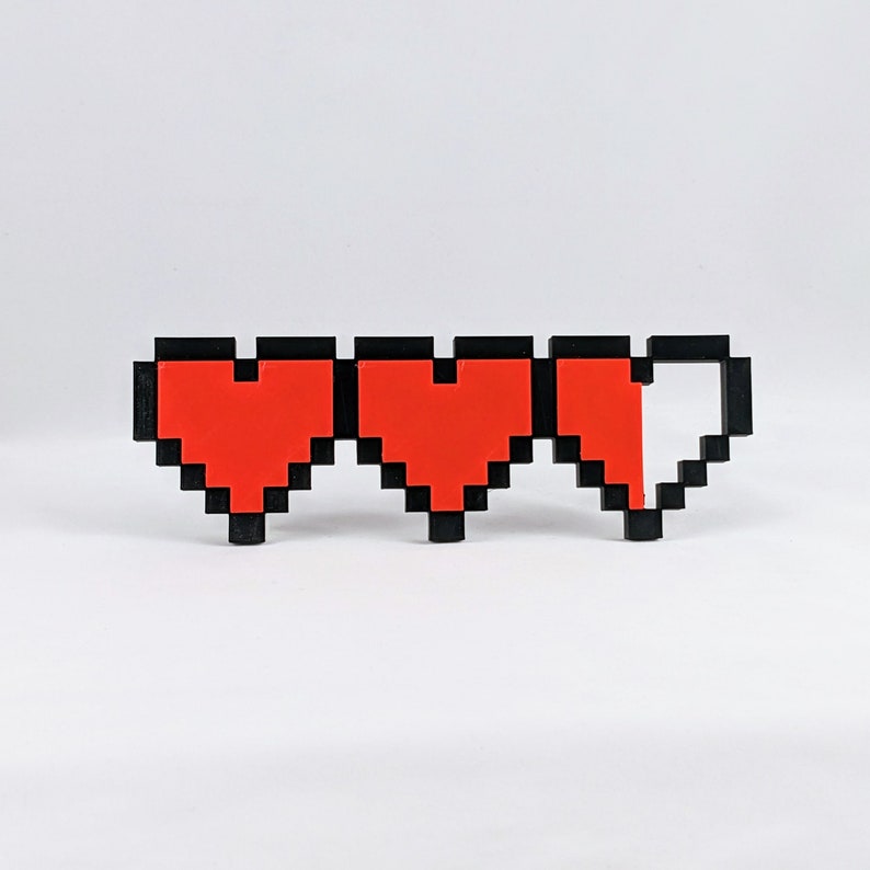 May include: Three pixelated hearts, two full and one half-full, in red with black outlines. The hearts are arranged horizontally.