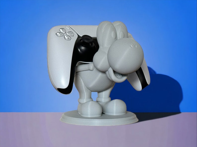 May include: A white 3D printed figurine of a cartoon character holding a white and black video game controller. The figurine is standing on a round base.