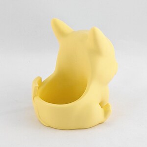 May include: A yellow ceramic planter shaped like a cartoon character. The planter has a small opening on the top for planting.