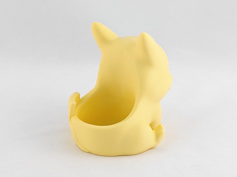 May include: A yellow ceramic planter shaped like a cartoon character. The planter has a small opening on the top for planting.