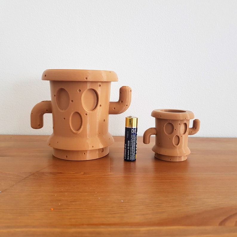 May include: Two brown ceramic cactus-shaped planters, one larger than the other, with a single AA battery for scale.