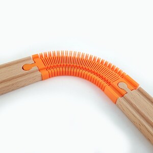 May include: A wooden train track with an orange flexible connector piece. The connector piece is made of a series of interlocking orange plastic pieces that allow the track to bend.
