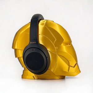 K&ouml;nnte beinhalten: Schwarze Over-Ear-Kopfh&ouml;rer mit dem Schriftzug "SONY" an der Seite, die auf einem goldfarbenen, helmf&ouml;rmigen St&auml;nder ruhen.