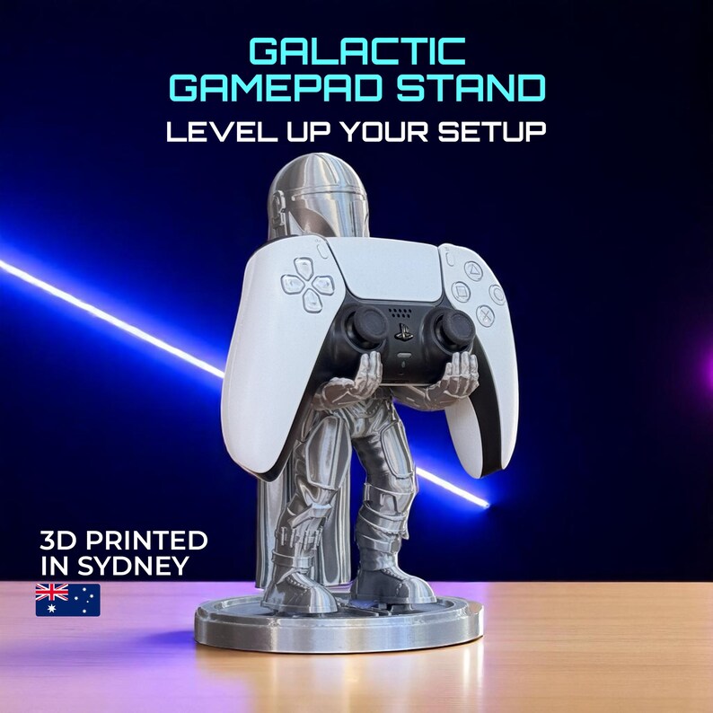 Pode incluir: Um suporte de gamepad prateado impresso em 3D em forma de personagem segurando um controle branco e preto. O suporte tem uma base redonda e o texto "GALACTIC GAMEPAD STAND LEVEL UP YOUR SETUP" &eacute; exibido em azul.