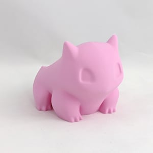 May include: A pink 3D printed figurine of a Pokemon character. The figurine is sitting on a white surface.