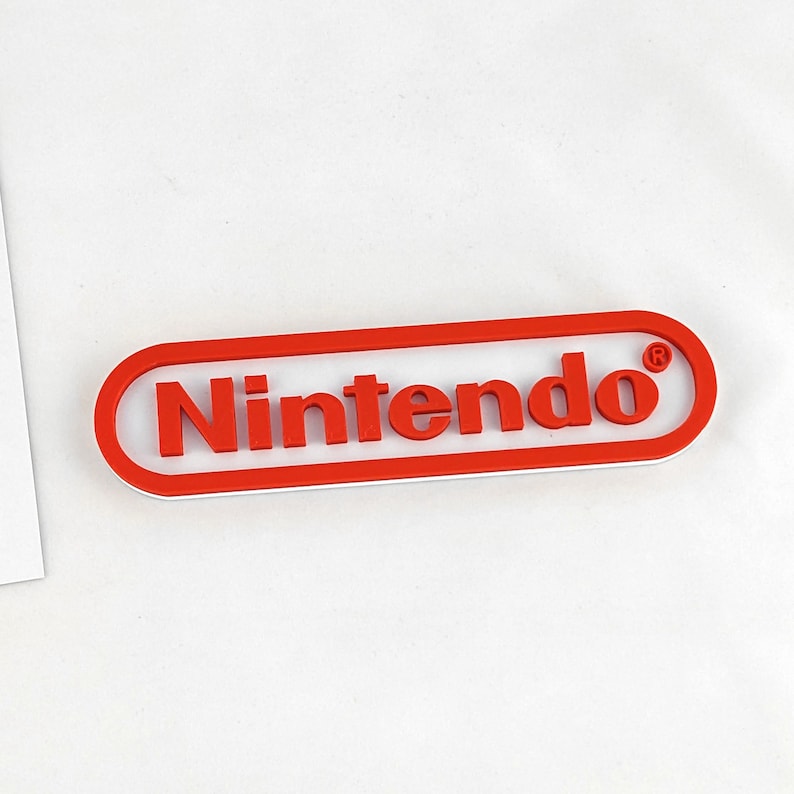 May include: A red and white plastic Nintendo logo with a registered trademark symbol.