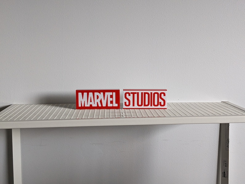 K&ouml;nnte beinhalten: Zwei rote Bl&ouml;cke mit wei&szlig;en Buchstaben. Der linke Block sagt "MARVEL" und der rechte Block sagt "STUDIOS".