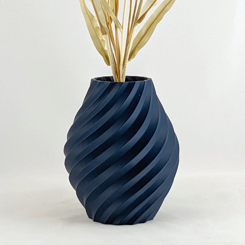 K&ouml;nnte beinhalten: Eine dunkelblaue Keramikvase mit einem wirbelnden, strukturierten Design. Die Vase ist leer.