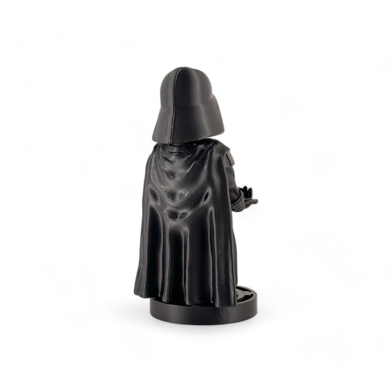 May include: Black Darth Vader figurine with a cape and a black base. The figurine is standing with its back to the camera.