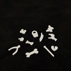 May include: White plastic shapes of various tools and objects, including a wrench, a bone, a bucket, a butterfly, a lightning bolt, a heart, a pair of pliers, and a stick.
