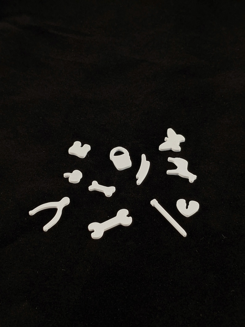 May include: White plastic shapes of various tools and objects, including a wrench, a bone, a bucket, a butterfly, a lightning bolt, a heart, a pair of pliers, and a stick.