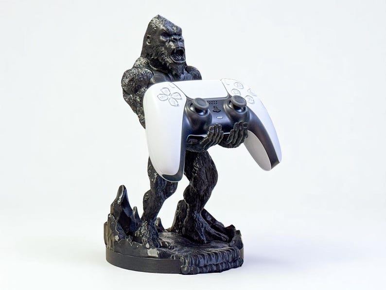 May include: A black gorilla statue holding a white and black video game controller. The statue has a textured finish and is mounted on a black base. The controller has a sleek, modern design.