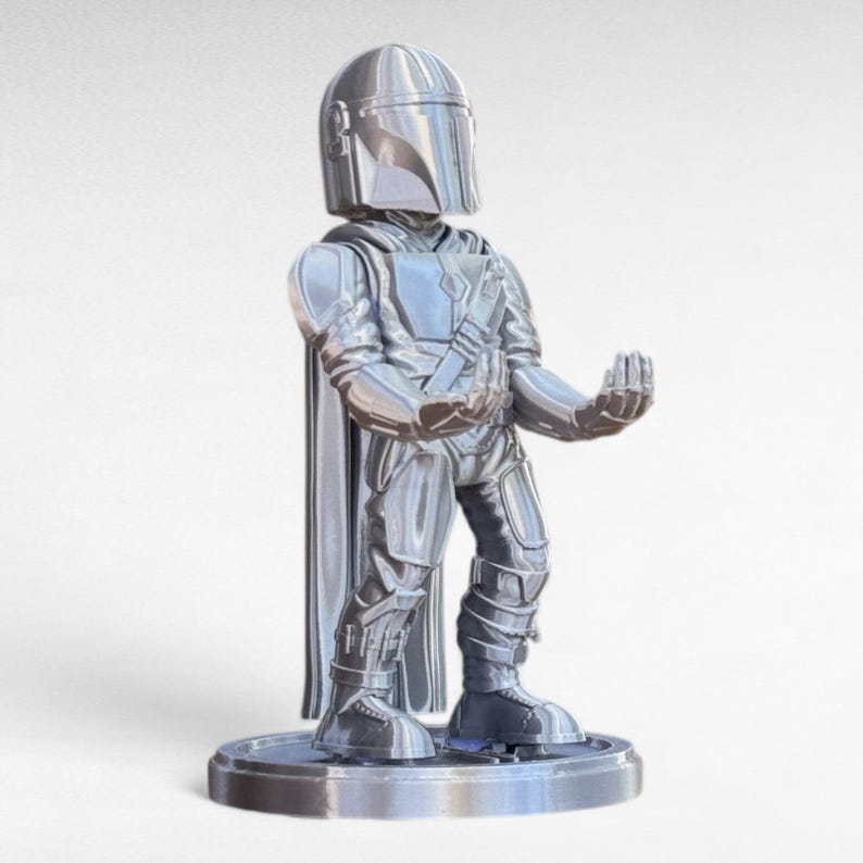 Pode incluir: Uma estatueta prateada de um personagem de uma s&eacute;rie de fic&ccedil;&atilde;o cient&iacute;fica. A figura est&aacute; usando um capacete, armadura e capa. Est&aacute; em p&eacute; sobre uma base circular com os bra&ccedil;os estendidos.