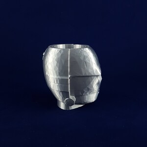 May include: A silver-coloured, geometrically-shaped planter with a textured surface. The planter is designed to resemble a head with a single ear.